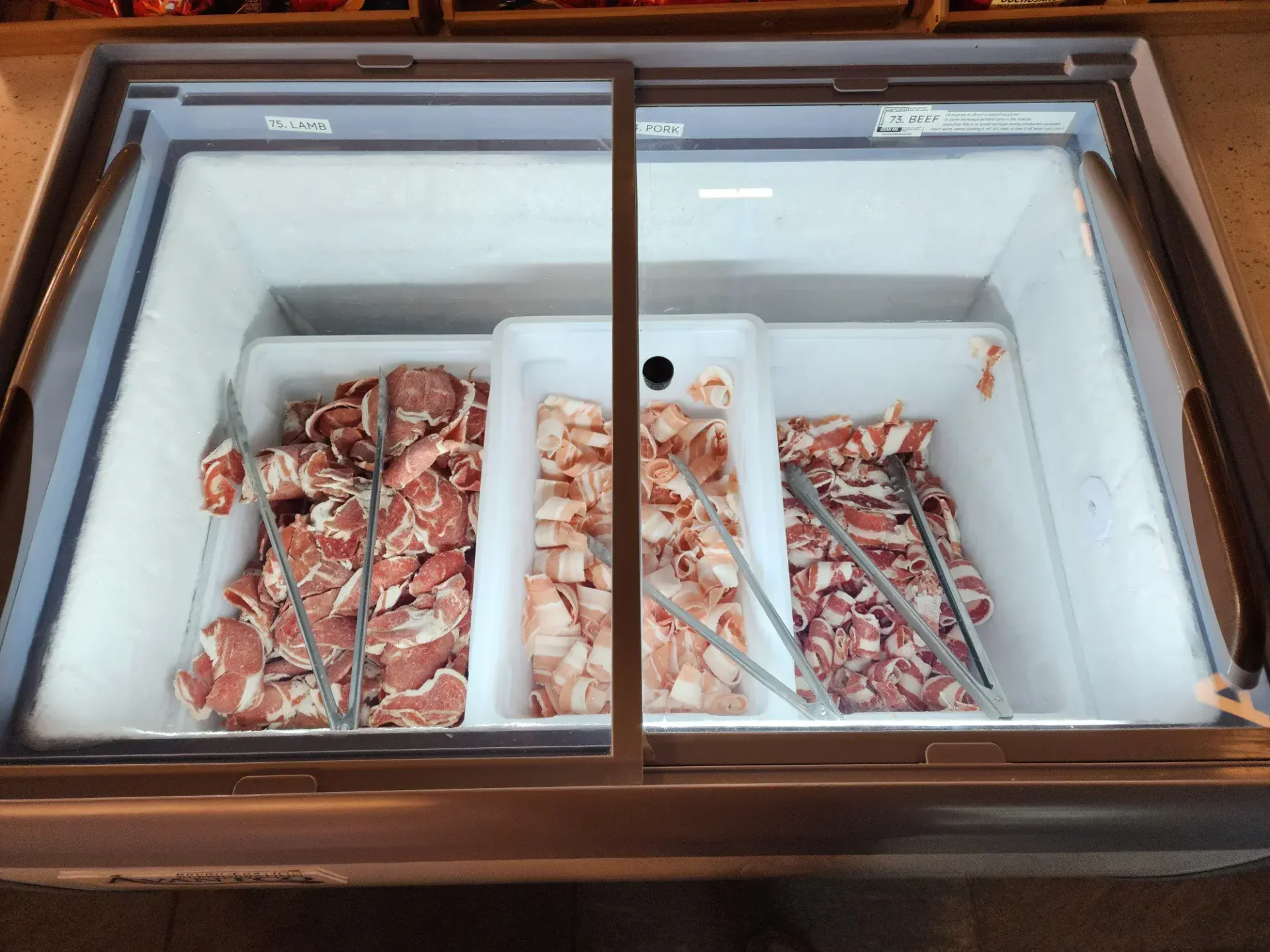 Premium shaved lamb, pork, and beef cuts in self-serve refrigerated display at Korean barbecue buffet