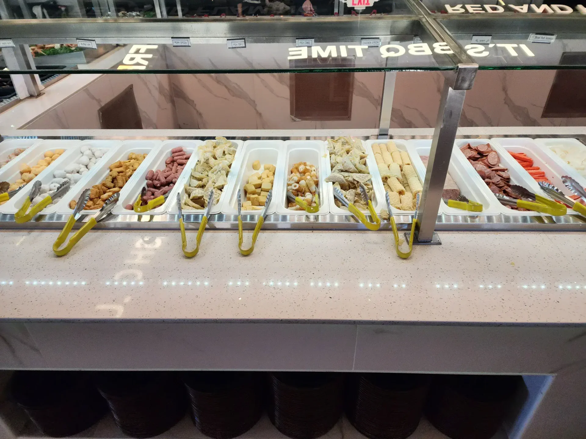 Korean BBQ buffet side dishes including rice cakes, fish cakes, sausage, and vegetables in serving trays