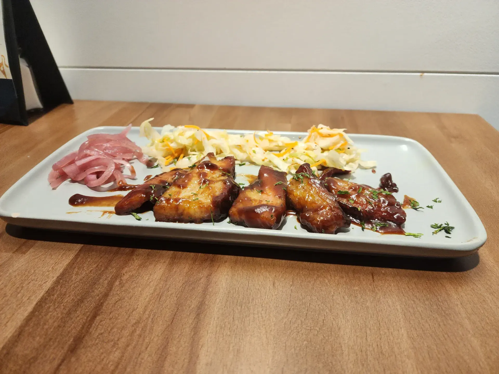 Plate of pork belly sliced up thin with picked red onion and some lettuce on the side.
